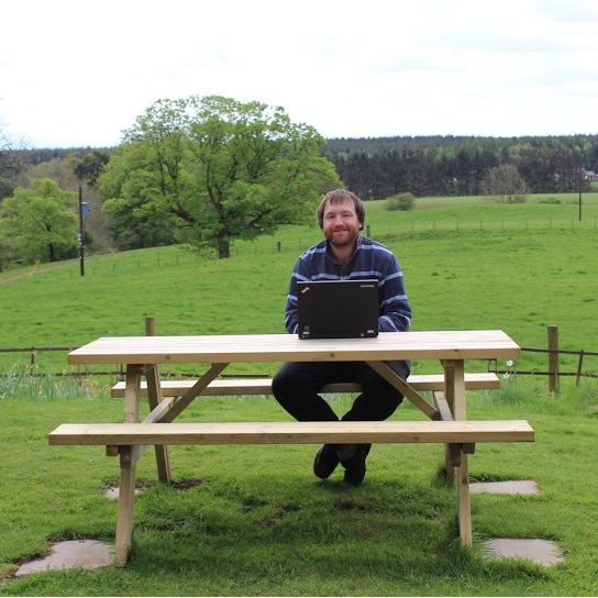 Robert Shepherd at a laptop on a park bench in the countryside.